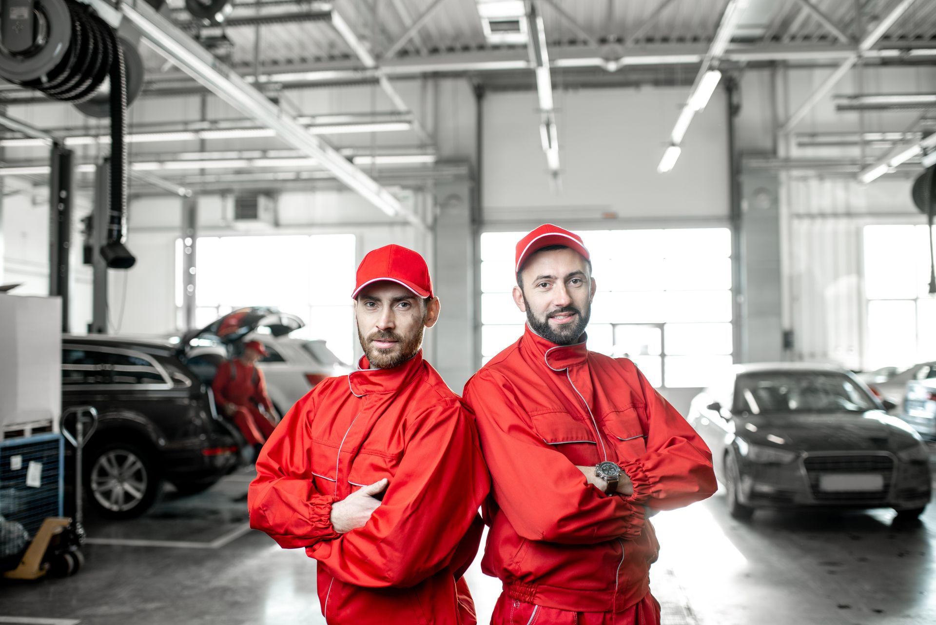 Deux mécaniciens en uniforme rouge, les bras croisés, dans un atelier de réparation automobile.