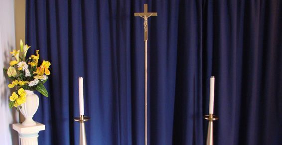 2 cierges et entre les deux un Christ sur sa croix placé en haut d'un bâton, le tout devant un rideau bleu foncé