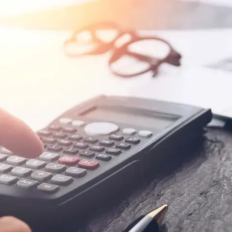 Una persona está usando una calculadora en una mesa de madera.