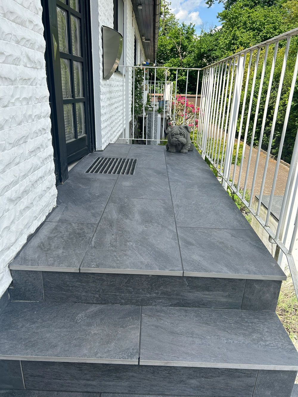 Eine schwarz geflieste Veranda mit Treppen, die zu einem weißen Backsteingebäude hinaufführen.