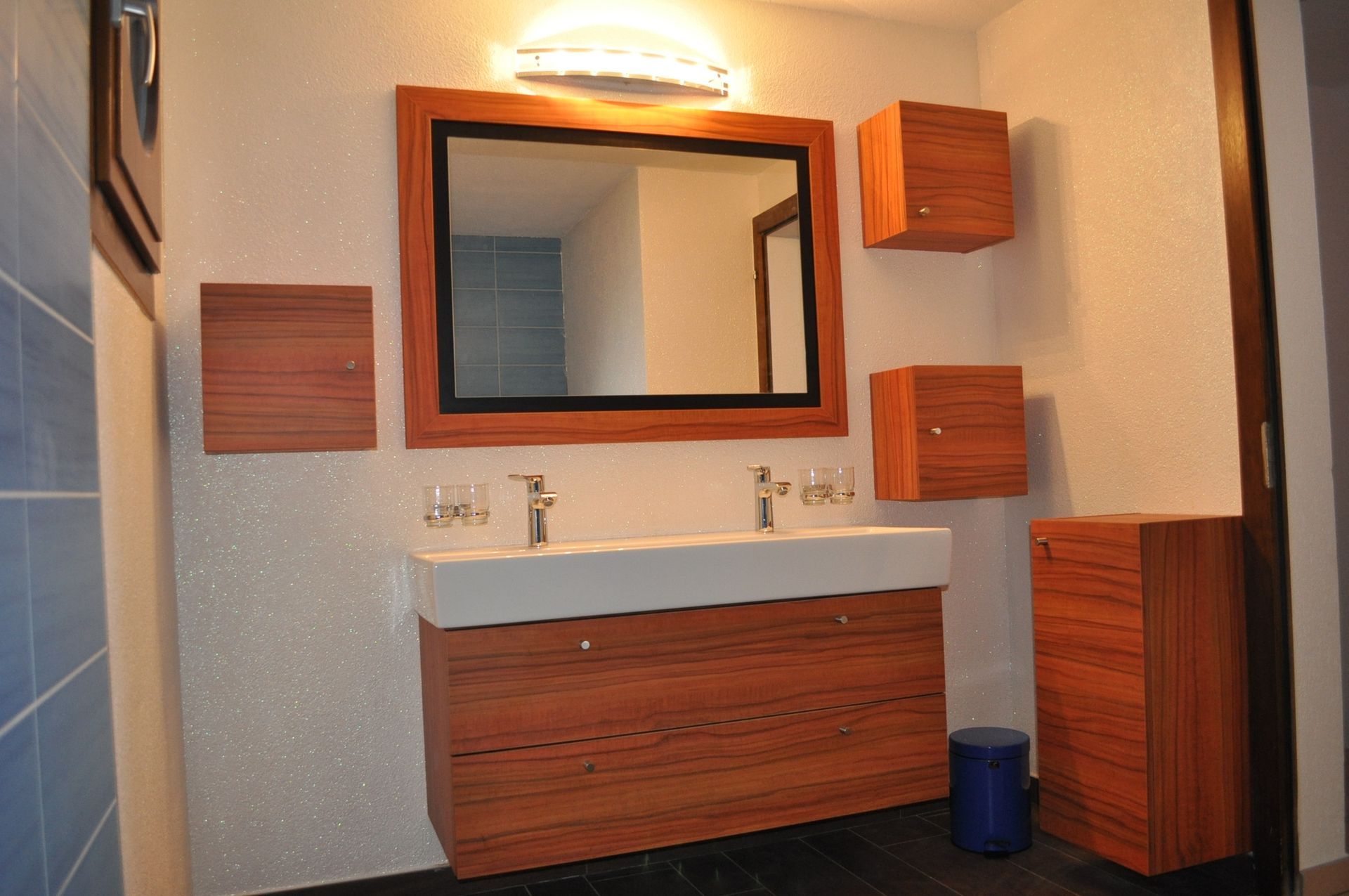 Salle de bain moderne avec meuble-lavabo en bois, miroir et meubles suspendus.