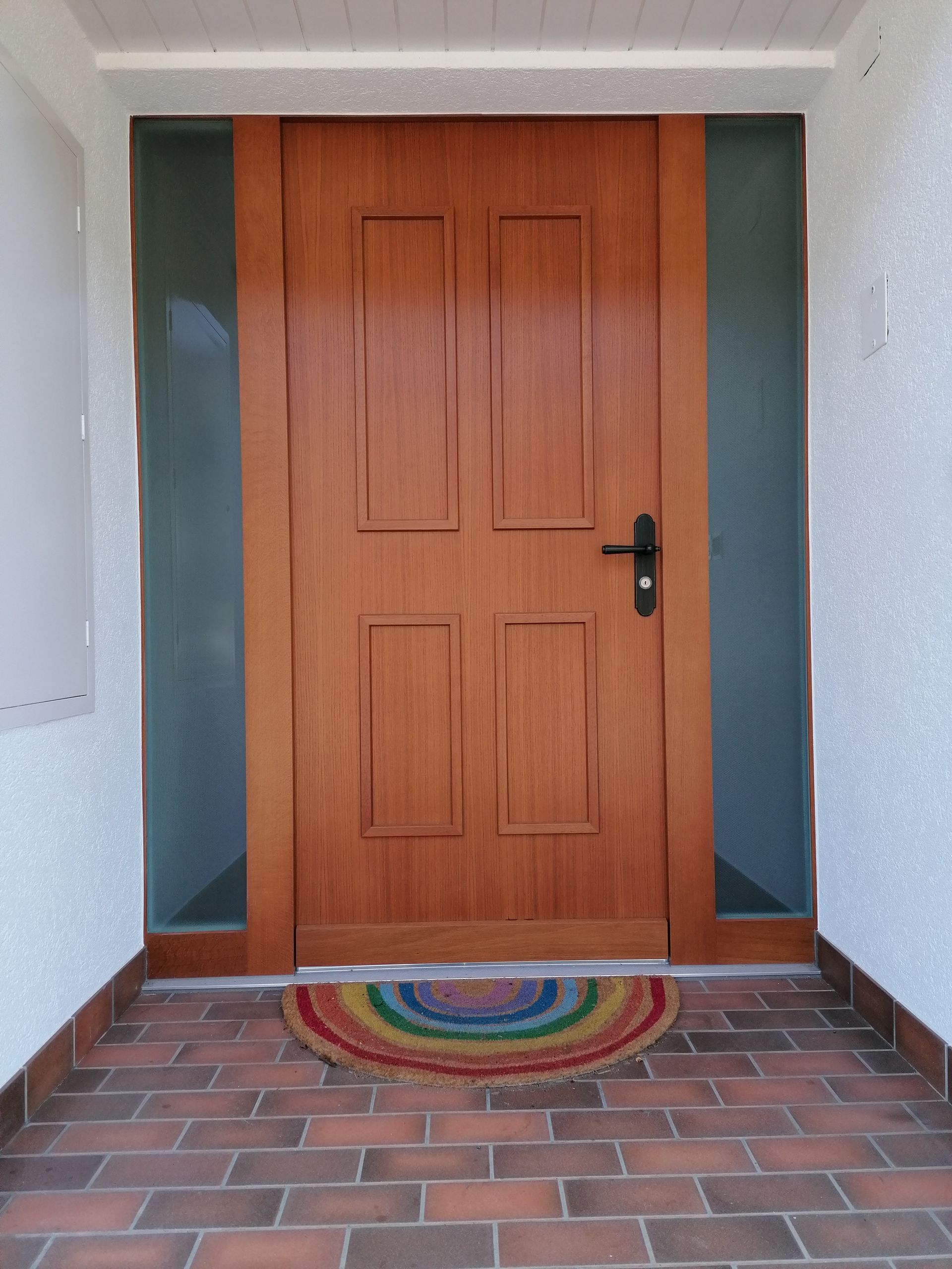 Porte d'entrée en bois avec panneaux latéraux en verre.
