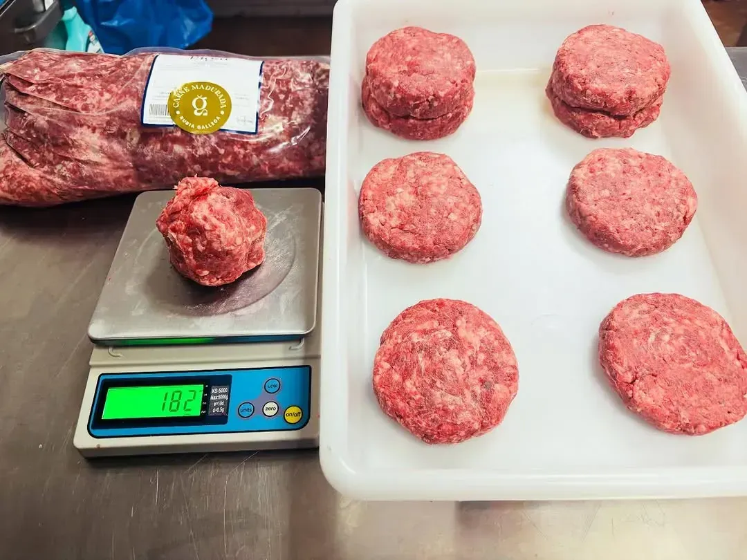 Hamburguesas de carne molida, una en una balanza (163g), seis en una bandeja y un paquete.
