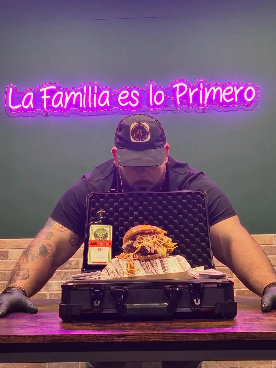 Hombre abre maletín con una hamburguesa, dinero en efectivo y alcohol debajo de un letrero de neón que dice