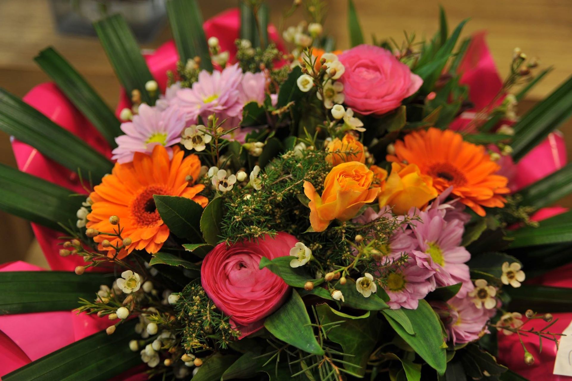 Bouquet coloré de fleurs roses, orange et jaunes, avec du feuillage vert et des touches de rouge