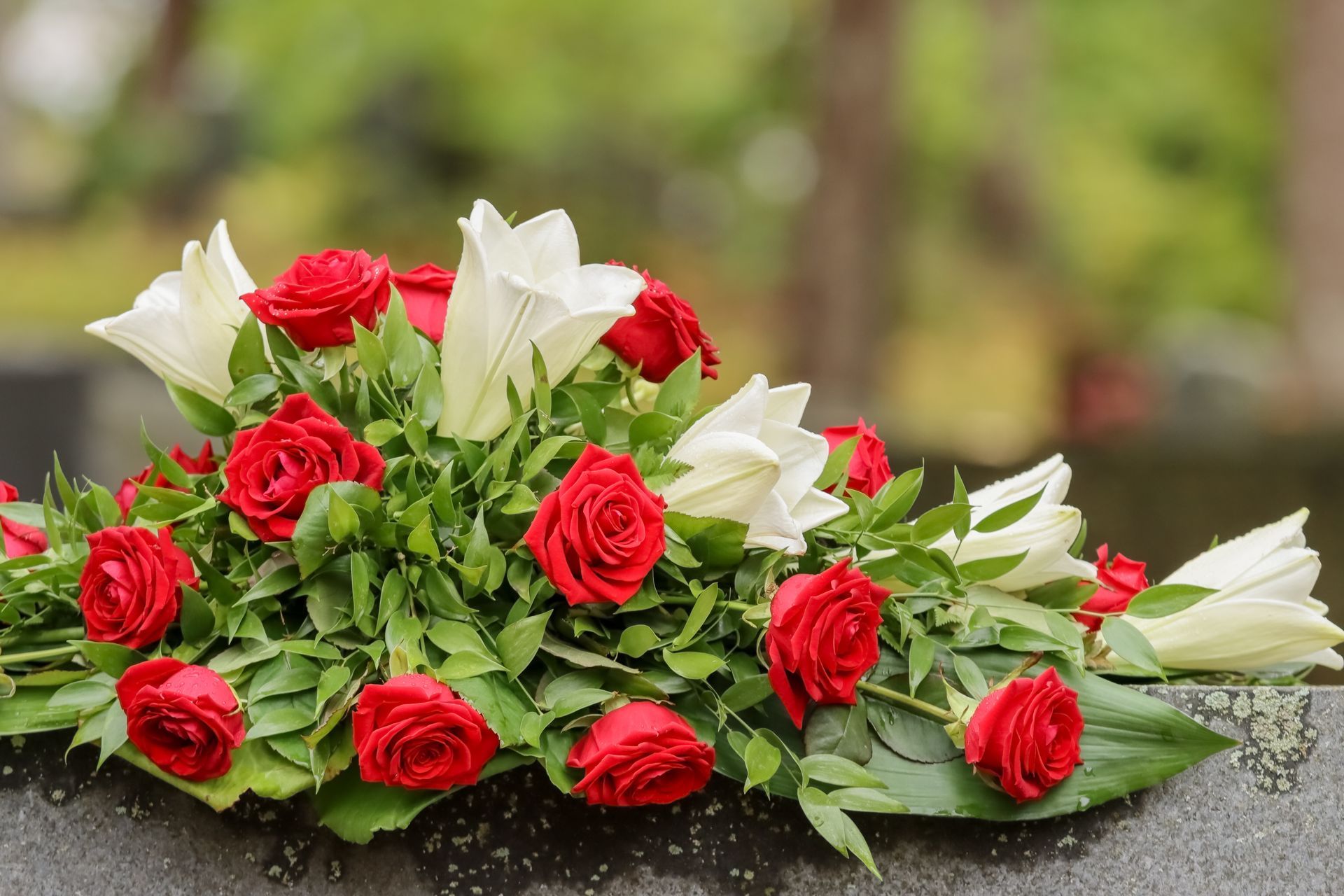 Composition de roses rouges et blanches avec des feuilles vertes, posée sur une surface en marbre en extérieur
