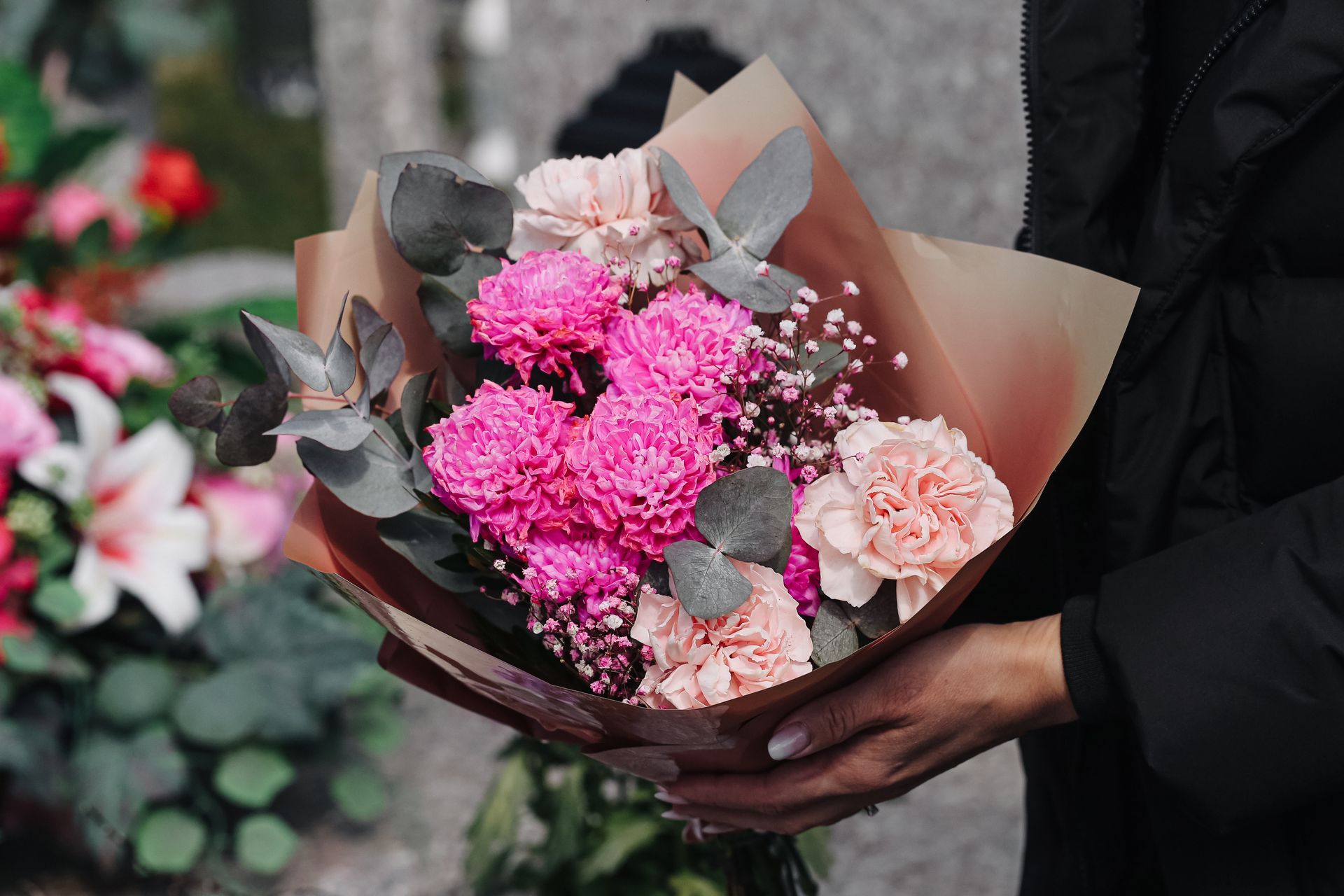 Une personne tenant un bouquet de fleurs roses et blanches enveloppées dans du papier marron et gris