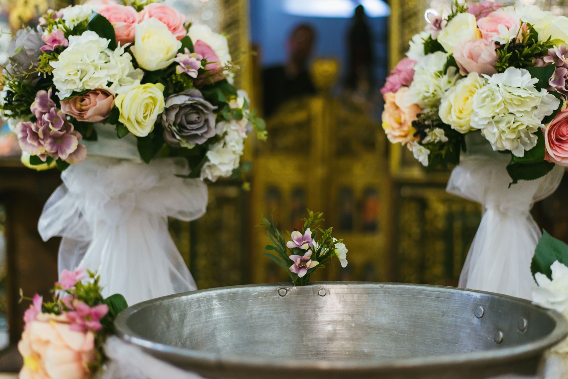 Deux bouquets de fleurs pastel encadrent une cuve baptismale en argent dans une église