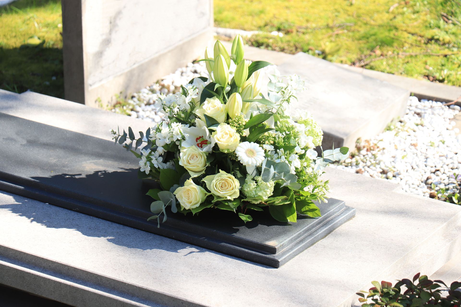 Bouquet de fleurs blanches posé sur une pierre tombale noire, en extérieur