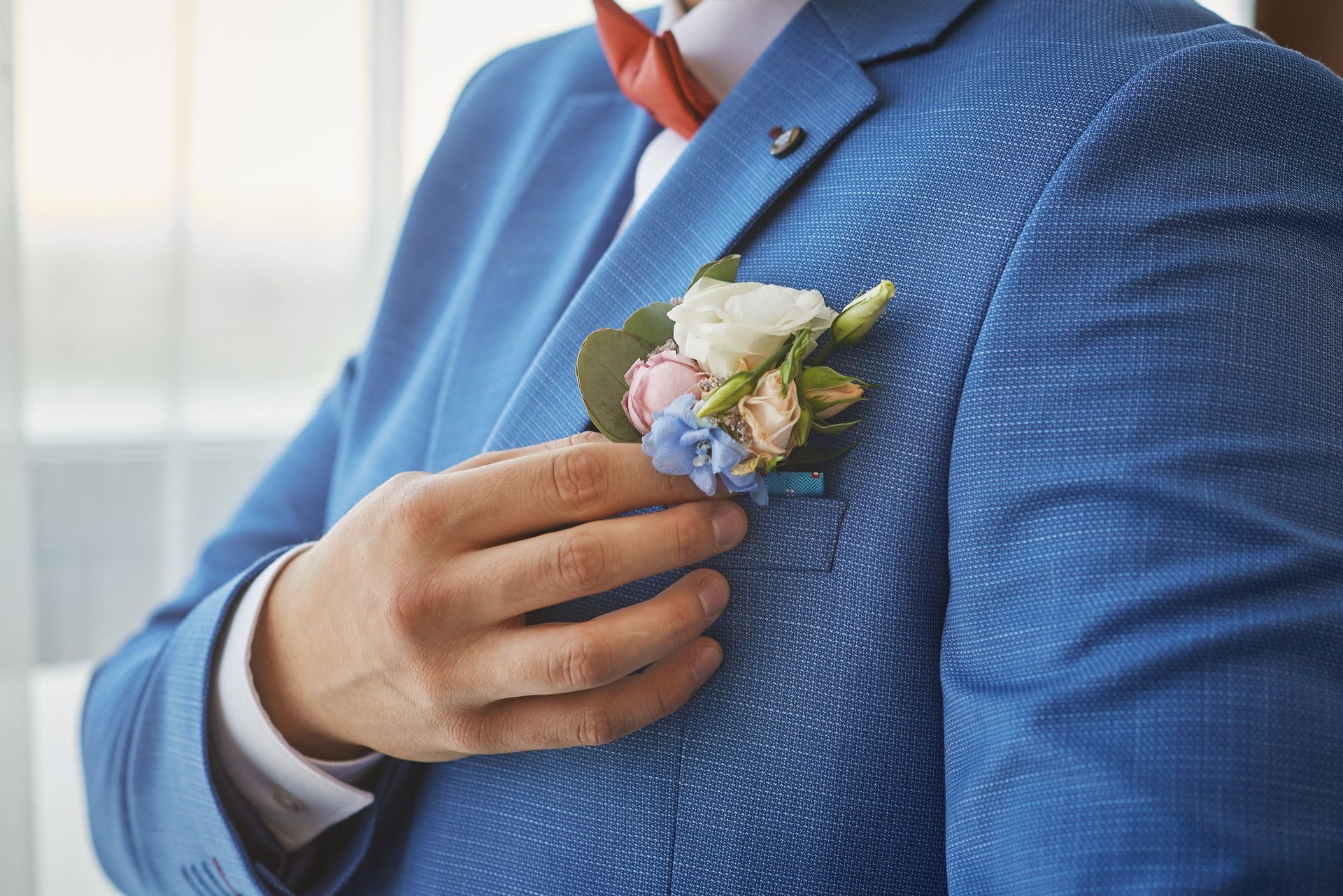 Une main épingle une boutonnière blanche et rose à la veste bleue d’un costume