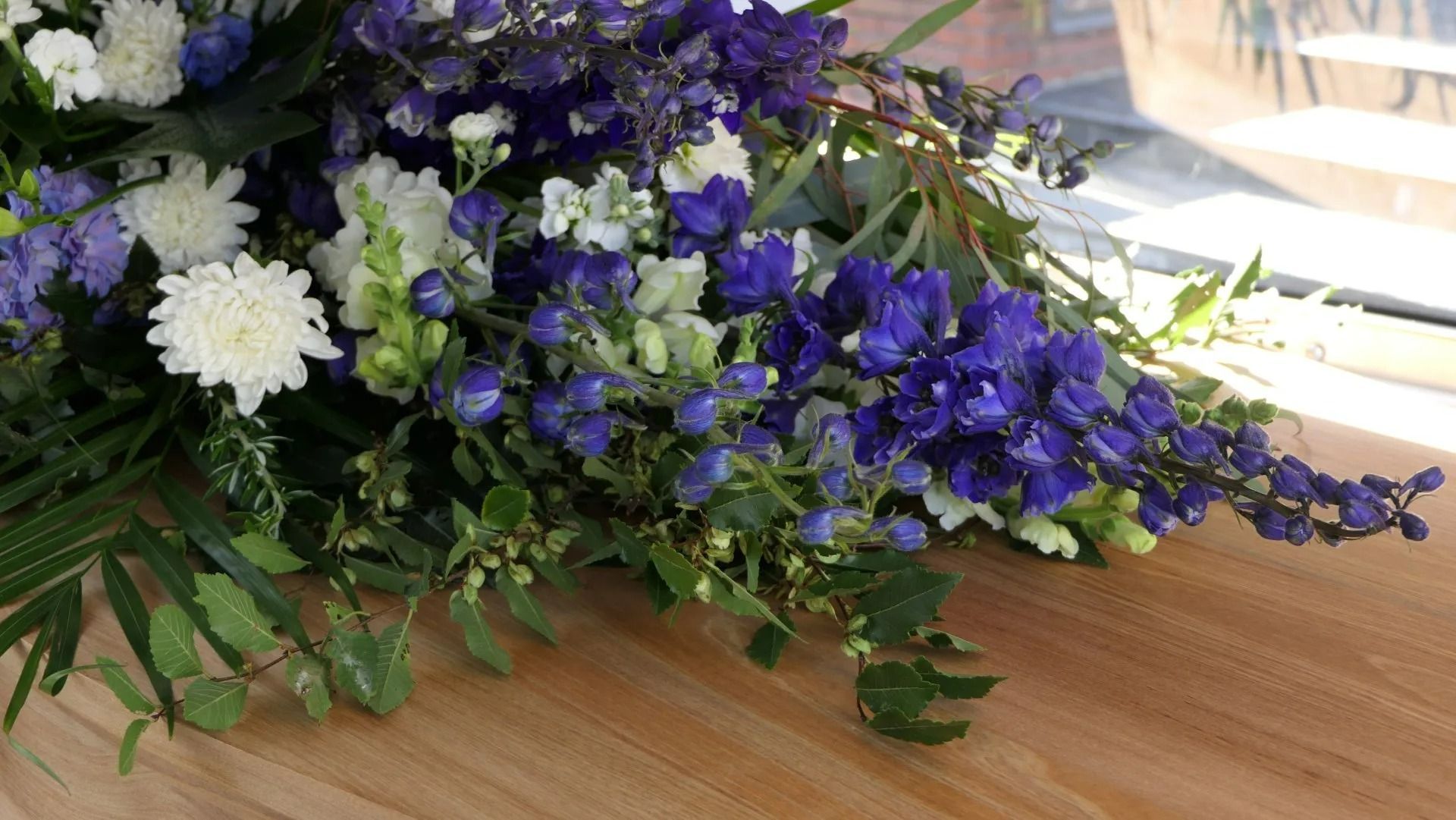 Composition florale bleue et blanche sur une table en bois, avec du feuillage vert