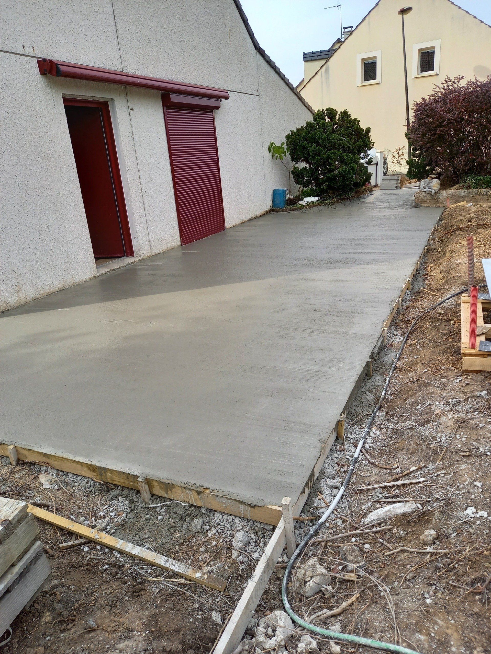 Chape en cour de construction devant une maison avec des volets roulants rouges