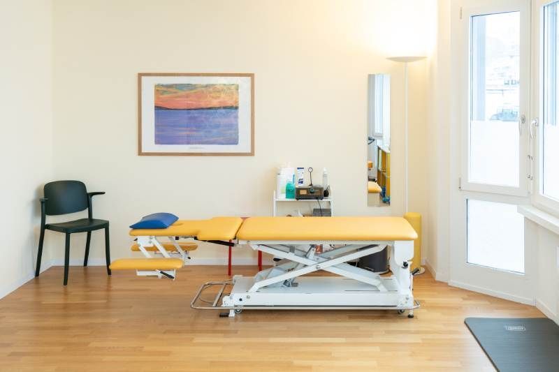 In der Mitte des Praxisraumes steht ein gelber Behandlungstisch. Foto von der Physiotherapie Kriens