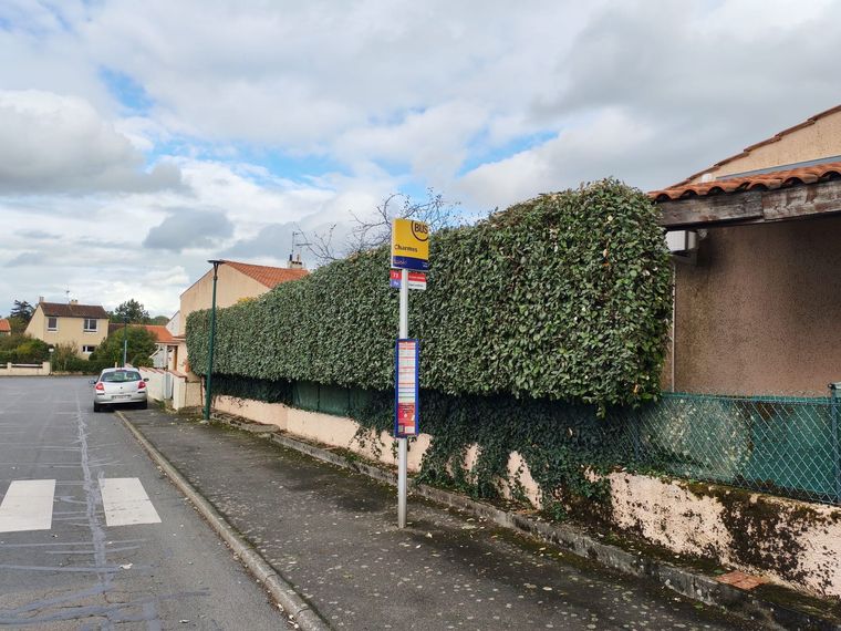 Rue de banlieue tranquille, bordée d'une haie, ciel nuageux et panneau de passage piéton.