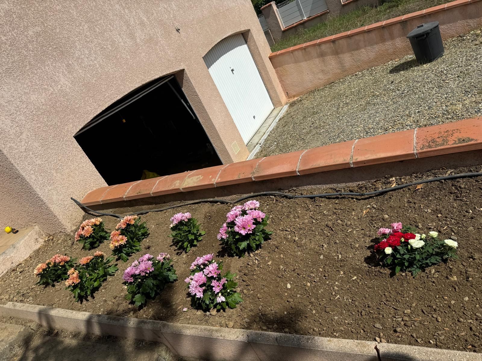 Parterre de fleurs roses et rouges le long d'un mur de briques, à côté de l'extérieur d'une maison