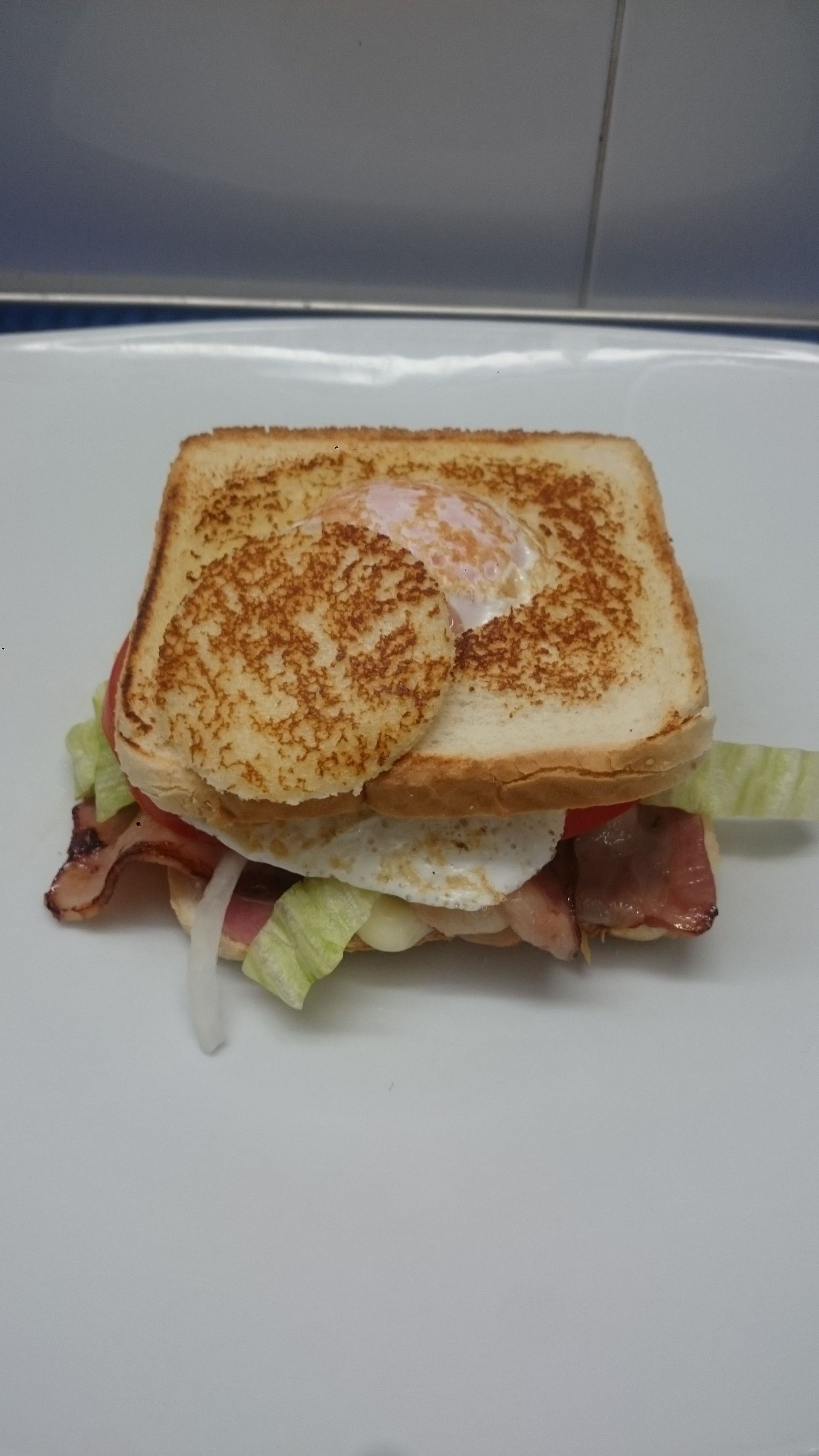 Un sándwich con huevos, tocino, lechuga y tomates en un plato blanco.