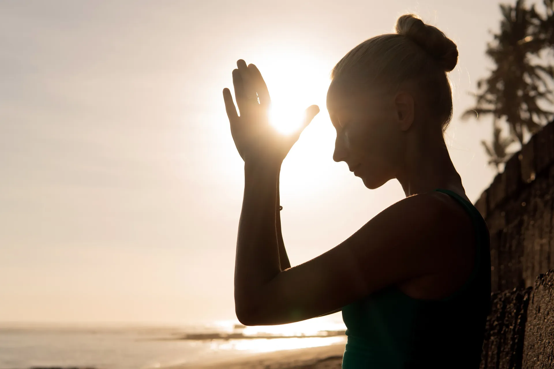 Silueta de una persona de perfil con la mano levantada contra una brillante puesta de sol en la playa.