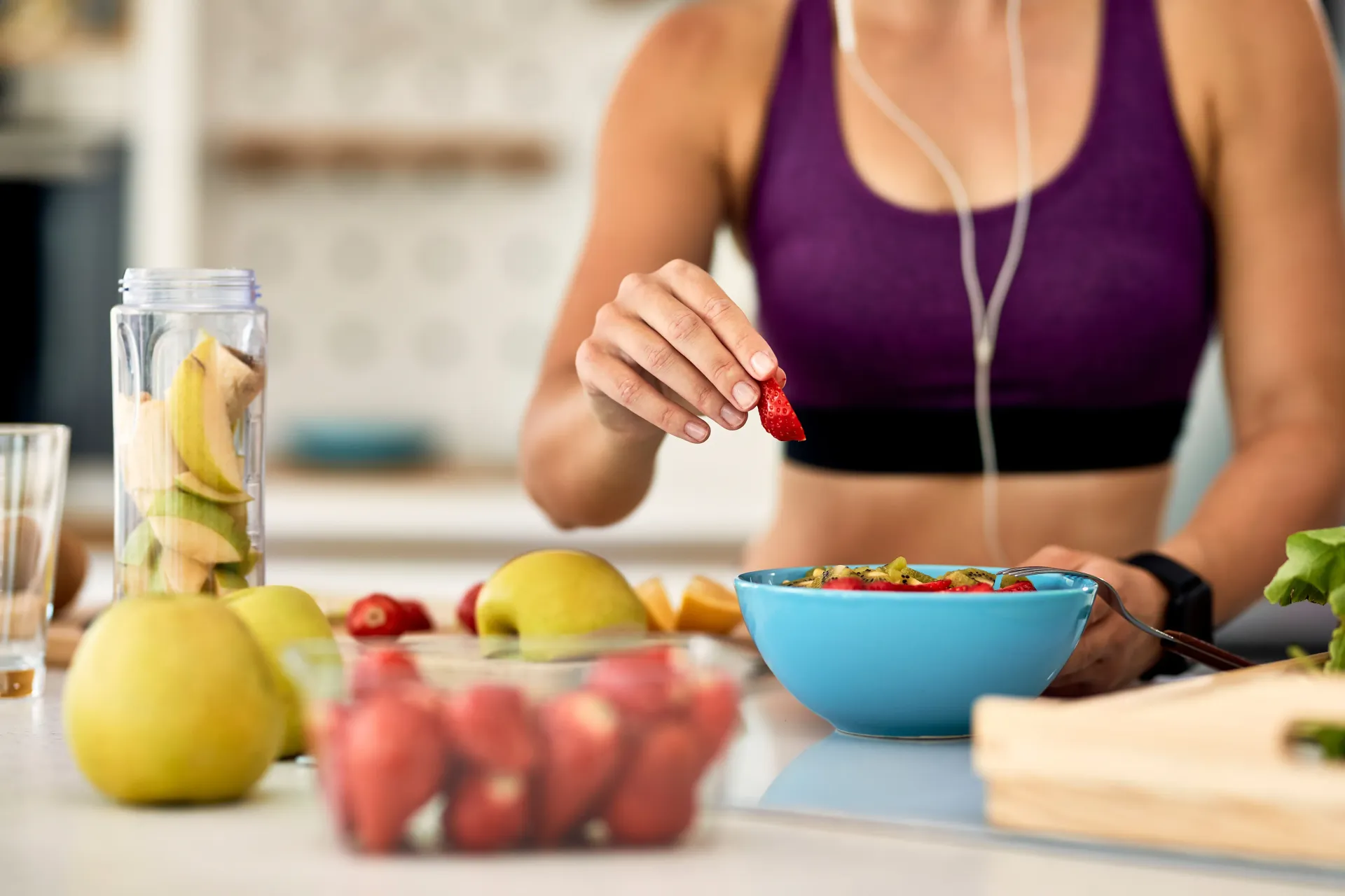 Mujer con top deportivo morado añadiendo bayas a un frutero en la encimera de la cocina.