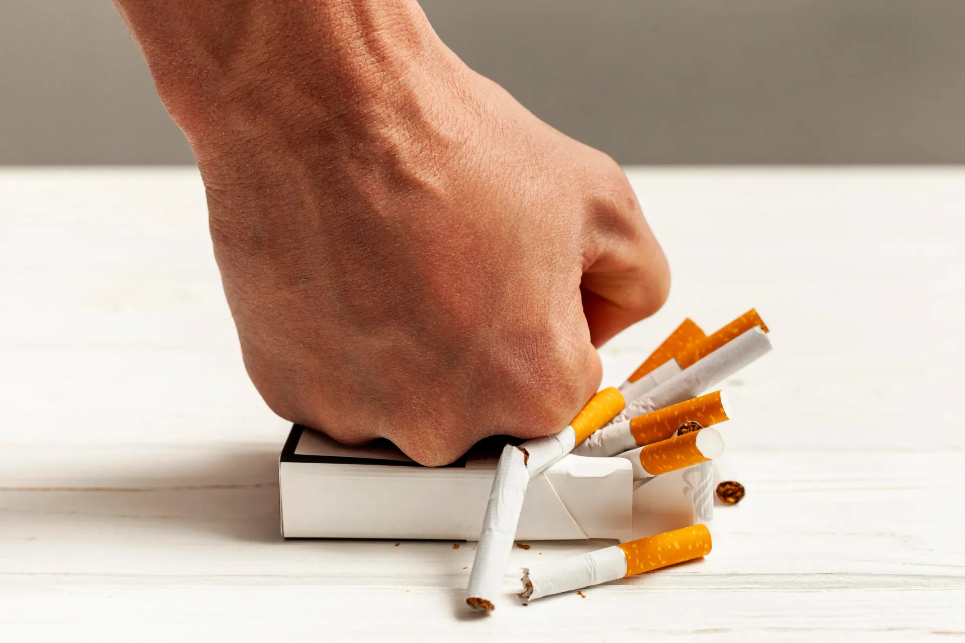 Aplastar a mano una pila de cigarrillos sobre una superficie blanca, con cigarrillos rotos y tabaco derramándose.