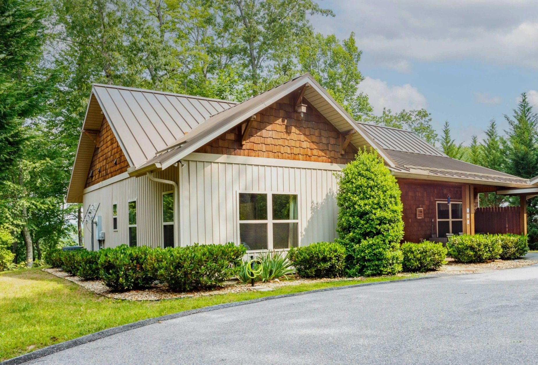 Cabin with a metal roof, cedar shake accents, and landscaped bushes along the drive.