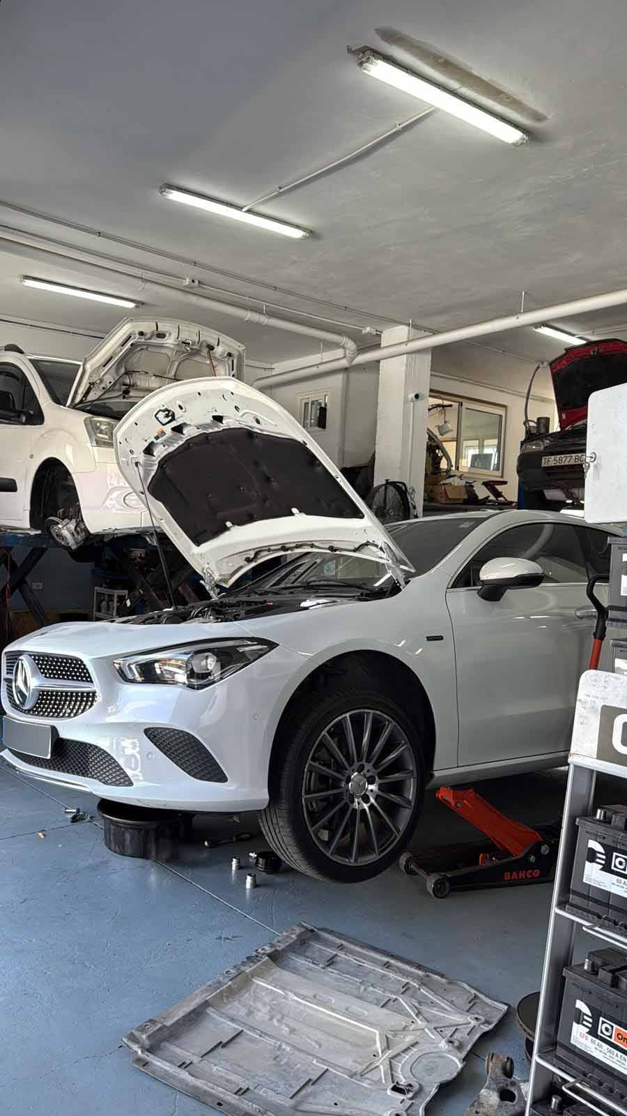 Se está trabajando en un coche blanco en un garaje con el capó abierto.