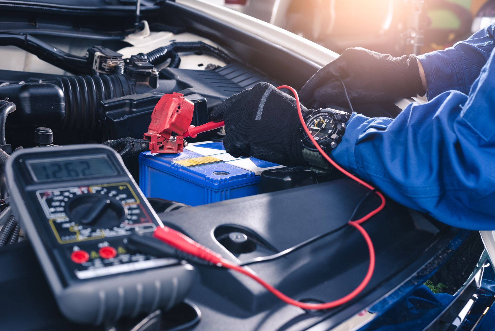 Mécanicien équipé d'un ampèremètre et faisant des vérifications sur la mécanique d'une voiture