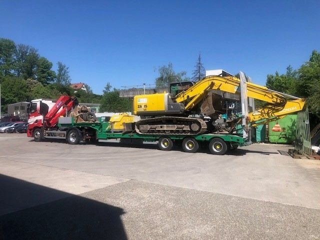 Gelber Baustellenlader auf einem Tieflader, der von einem gelben Lastwagen gezogen wird.