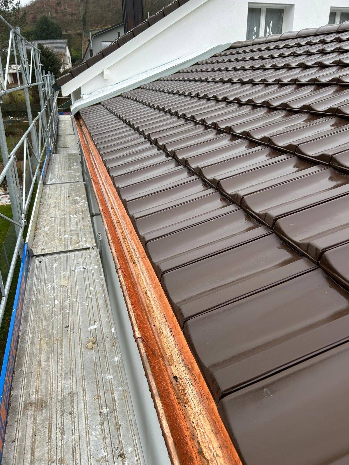 Ein Dach mit braunen Ziegeln und einer Kupferdachrinne darauf. Foto von Besi's Dachservice