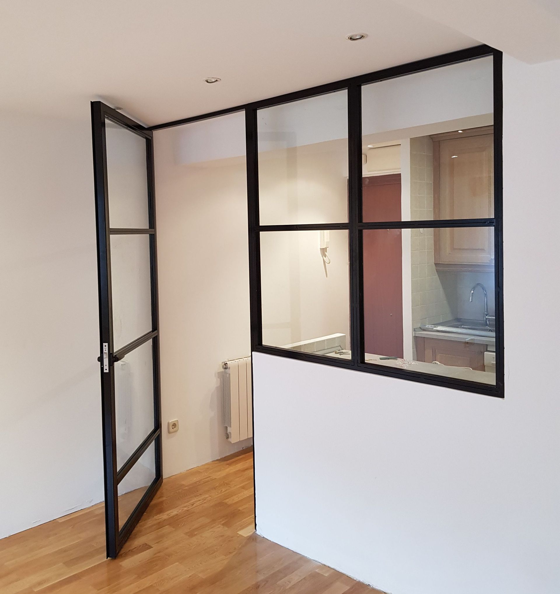 Una habitación con una pared de cristal y una puerta que conduce a una cocina.