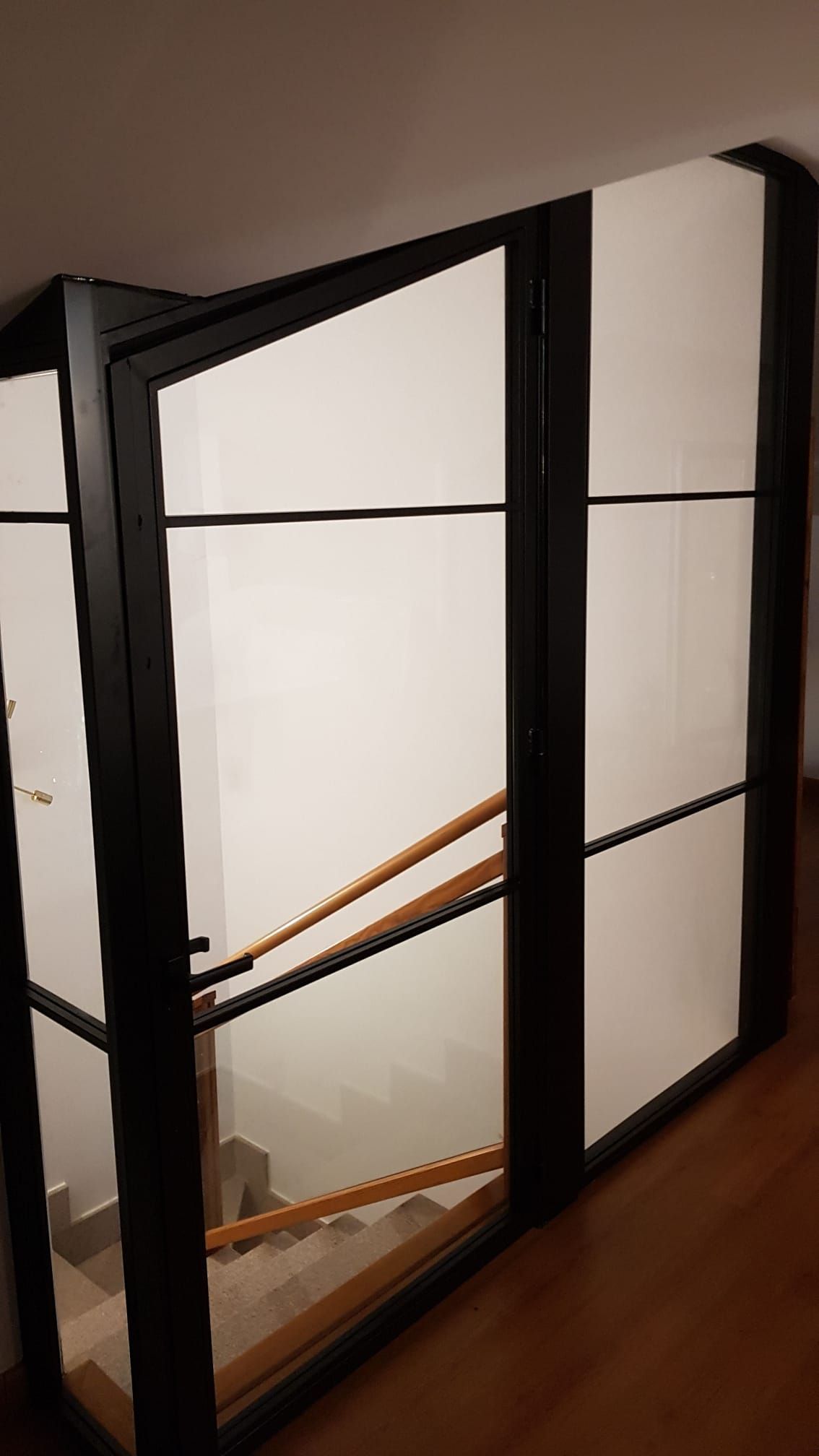 Hay una escalera detrás de una pared de vidrio con una barandilla de madera.