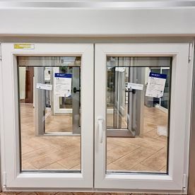 Una ventana blanca con dos puertas de vidrio está sobre un piso de baldosas en una habitación.