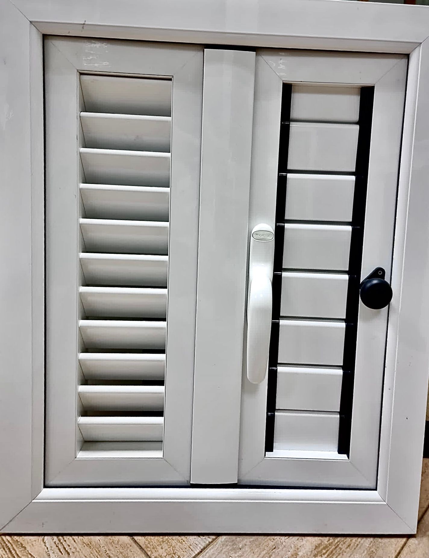 Una ventana blanca con contraventanas negras y una manija negra.