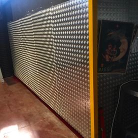 Una pared de metal con agujeros y una esquina amarilla en una habitación.