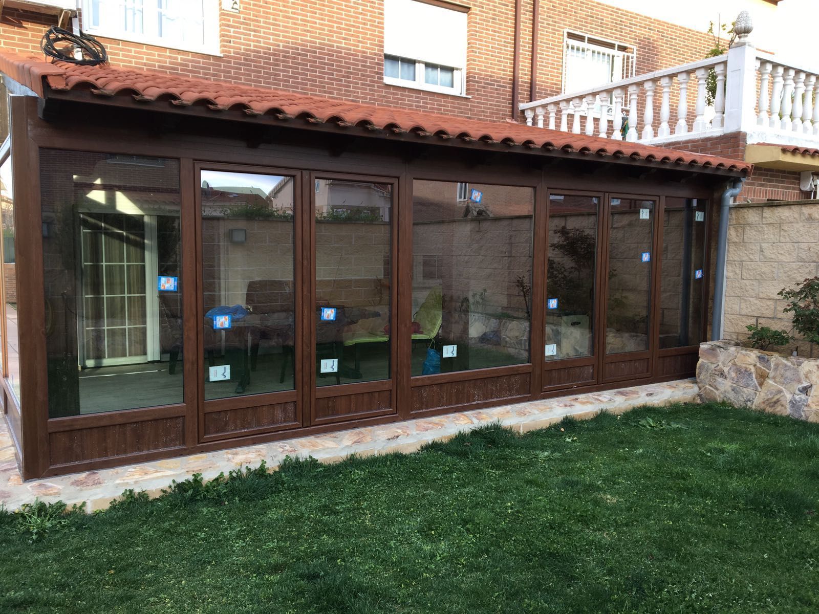 Una habitación grande con muchas ventanas y un techo de tejas rojas está en el patio trasero de una casa.