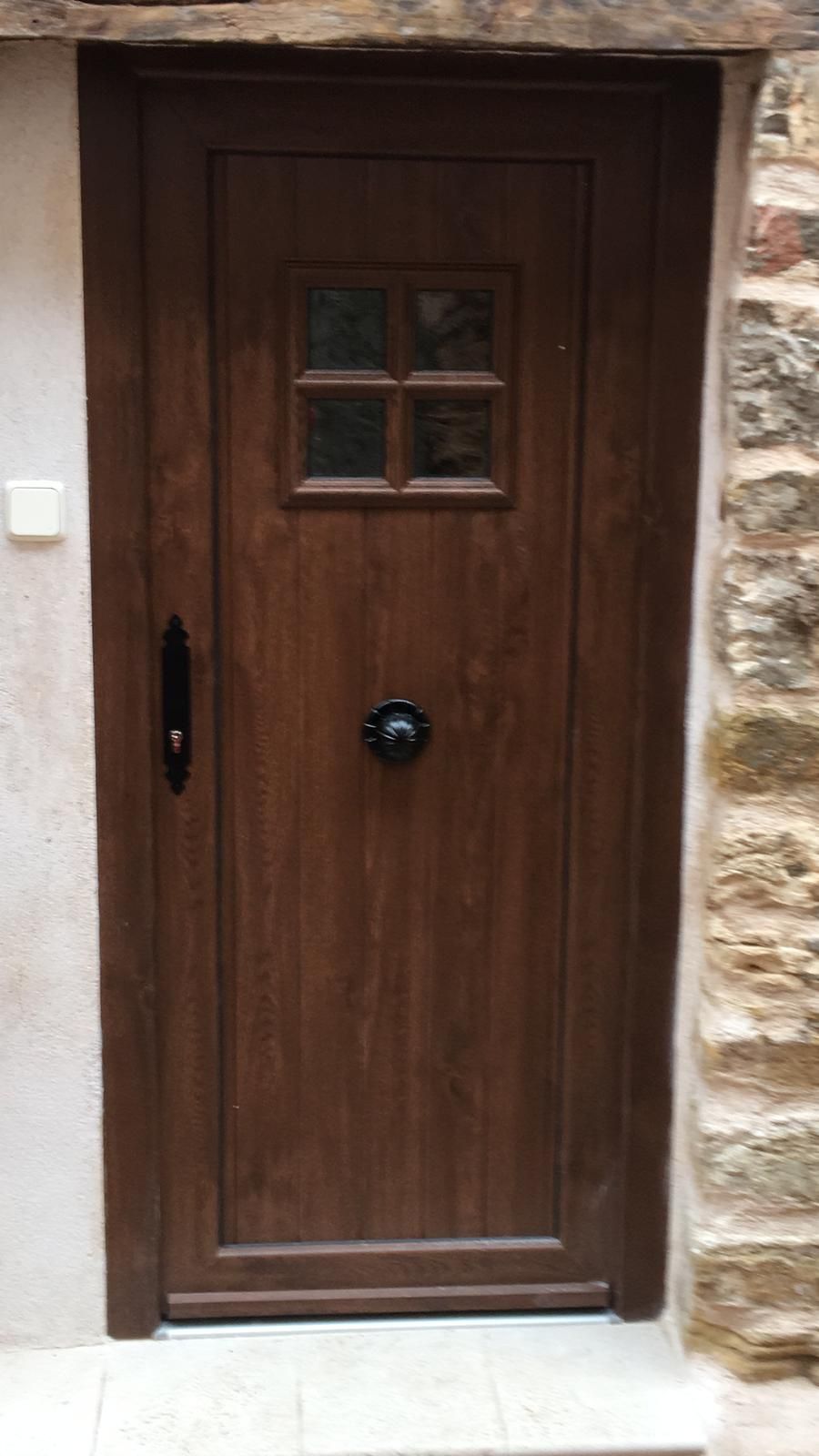 Una puerta de madera con cuatro ventanas está situada sobre una pared de piedra.