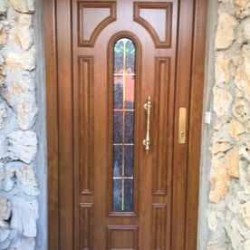 Una puerta de madera con una ventana de vidrio está al lado de una pared de piedra.