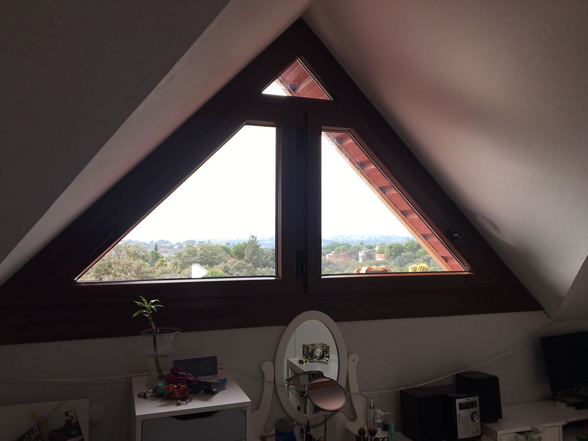 Un dormitorio con una ventana triangular y un tocador.