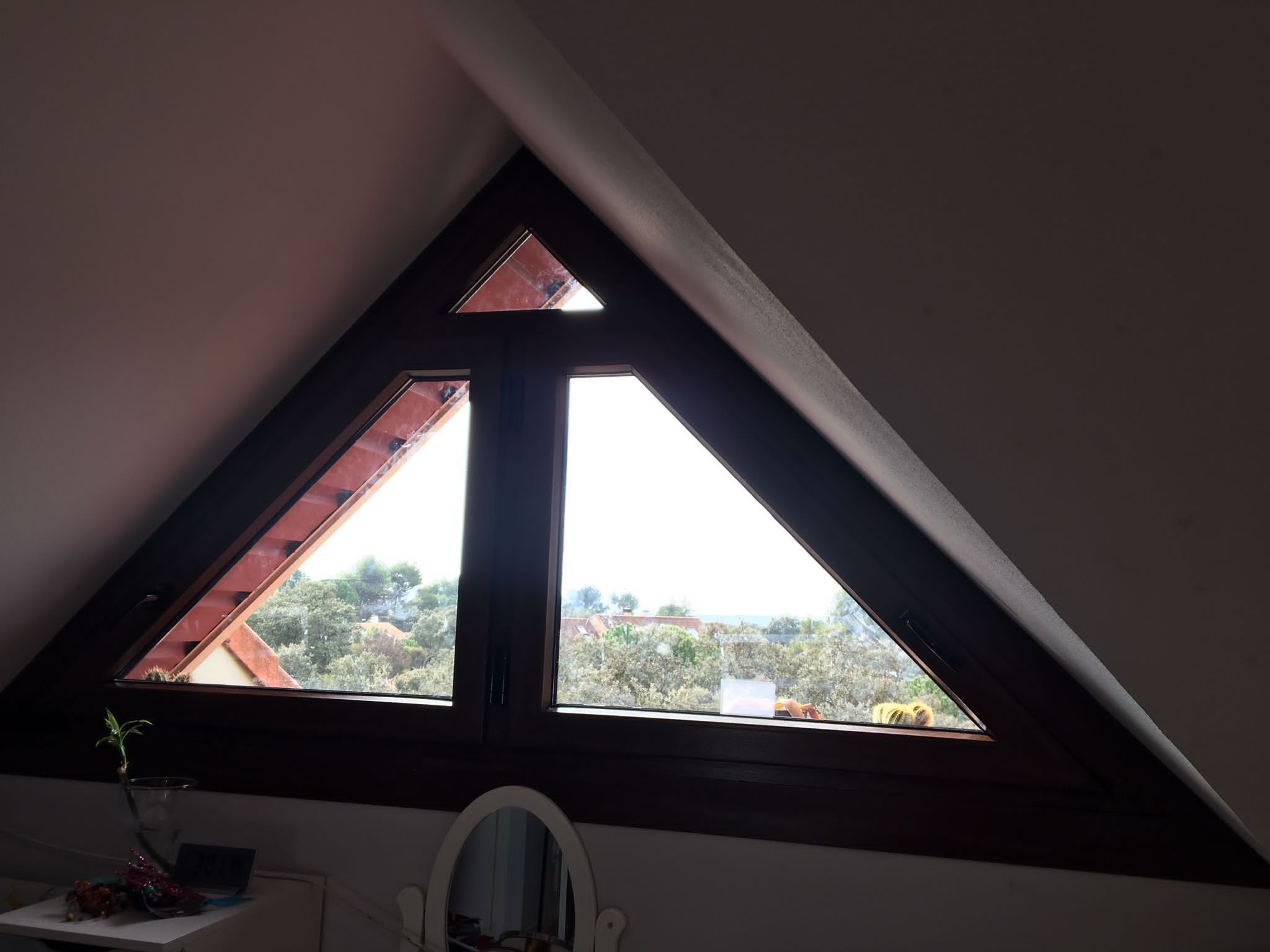 Una ventana en forma de triángulo en una habitación con un espejo.