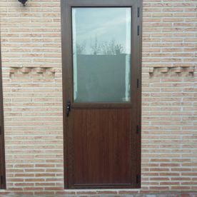 Una puerta de madera con una ventana de vidrio está en una pared de ladrillos.