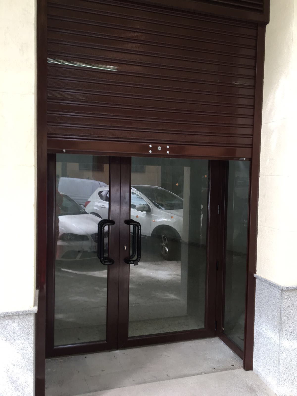 Una puerta con una persiana y un coche aparcado delante de ella.