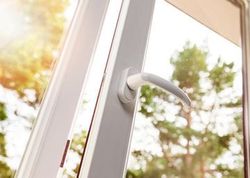 Un primer plano de una ventana abierta con una manija blanca y árboles en el fondo.