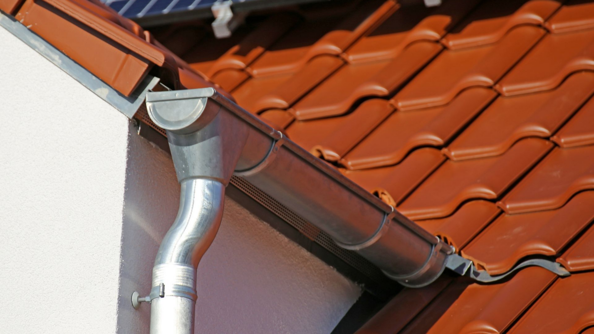 Gros plan sur le détail d'une gouttière posée sur la toiture en tuiles.