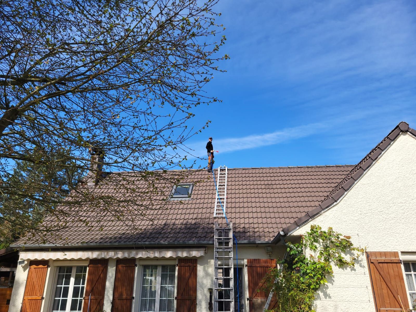 Professionnel debout sur le toit d'une maison avec une échelle en premier plan.