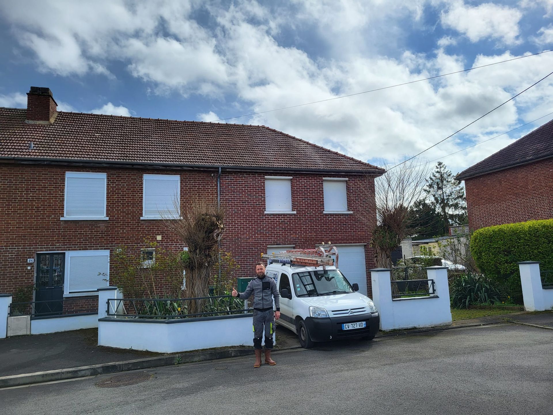 Professionnel devant une maison en briques et sa voiture à côté.