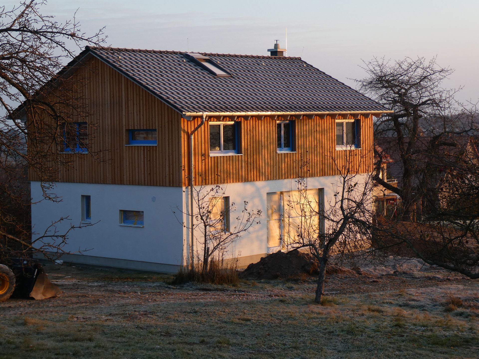 Zweigeschossiges Holzhaus mit weißem Sockel und sonniger Fassade