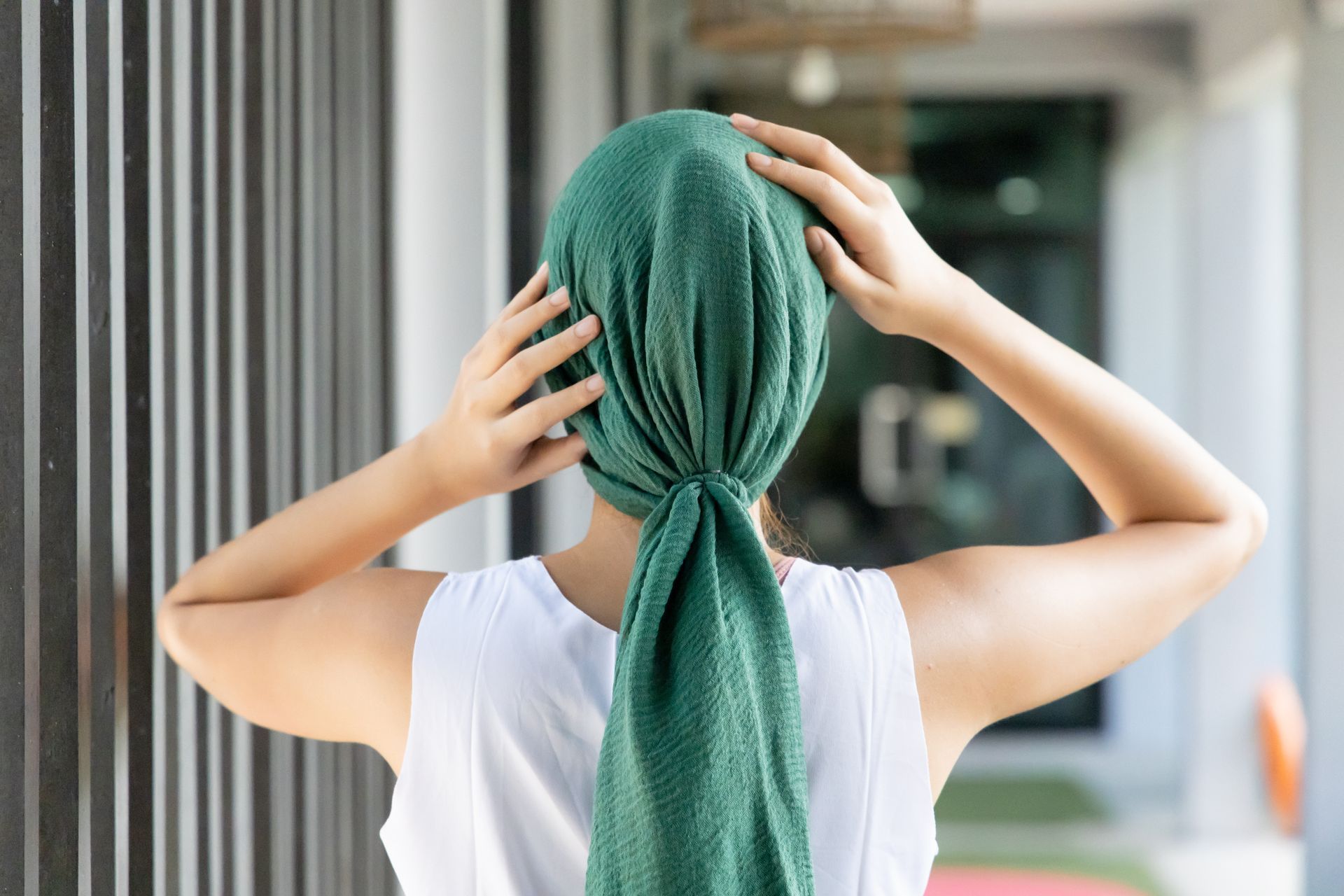 Une personne se noue une serviette verte sur la tête dans un couloir