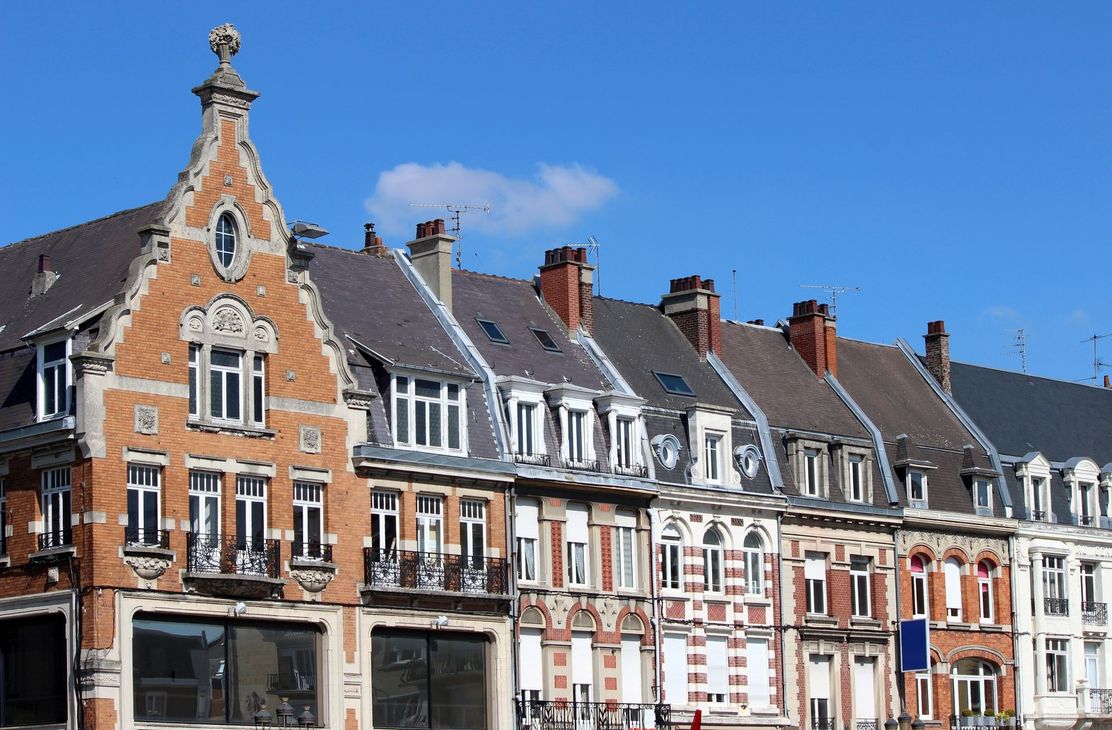 Rangée de maisons de ville en briques ornées, aux toits à pignons pentus, sous un ciel d'un bleu limpide.