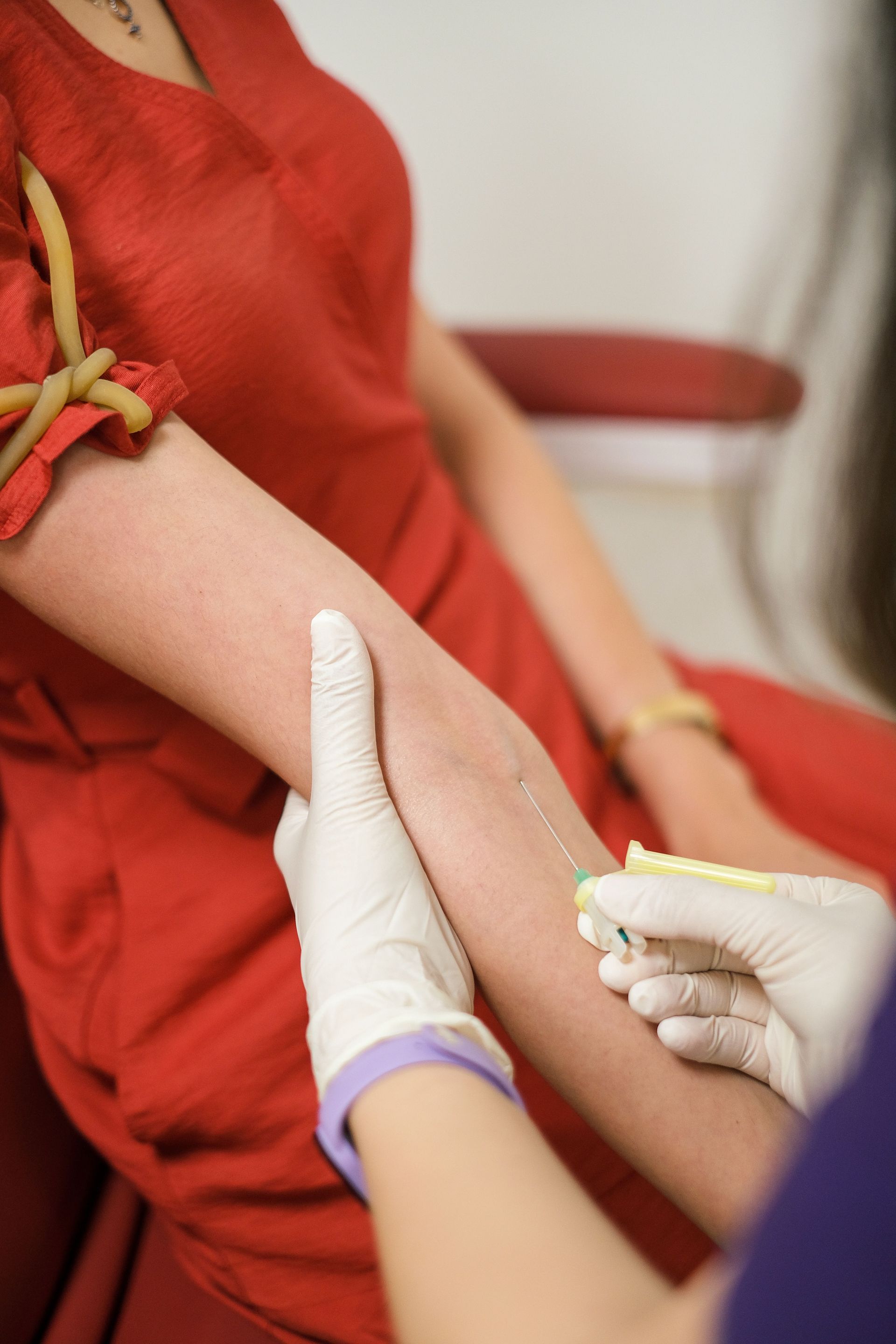 Des mains gantées administrent une injection à une personne en chemise rouge