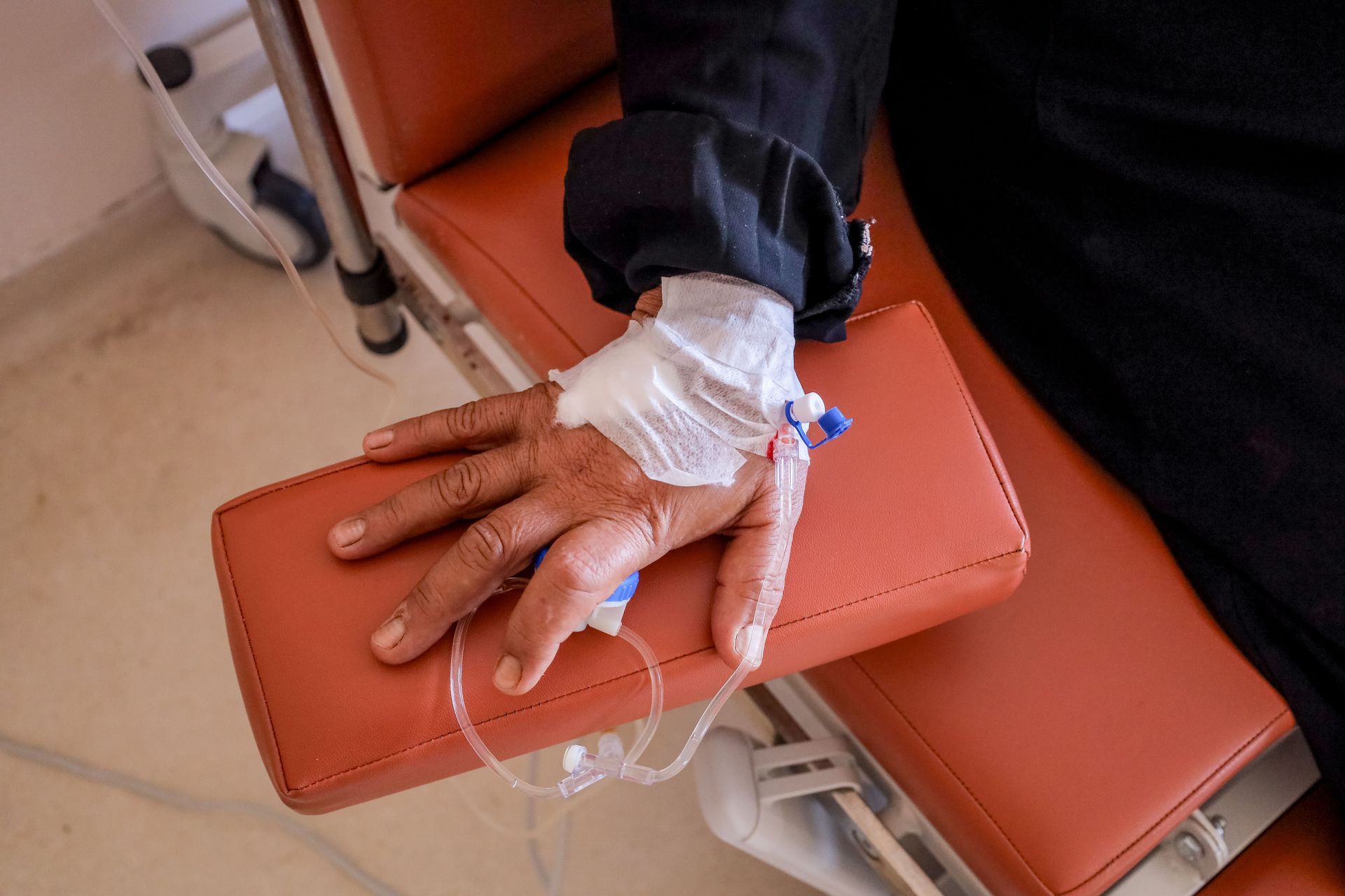 Main avec une tubulure de perfusion posée sur une chaise en vinyle marron dans un environnement clinique
