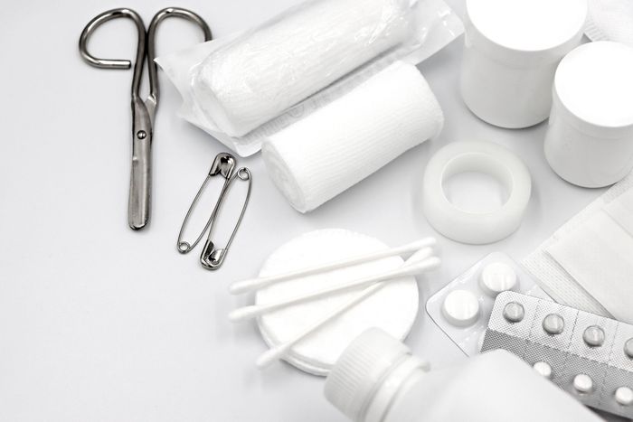 Fournitures médicales blanches assorties, notamment des pansements, de la gaze, des pinces à épiler et des plaquettes thermoformées, sur fond blanc.